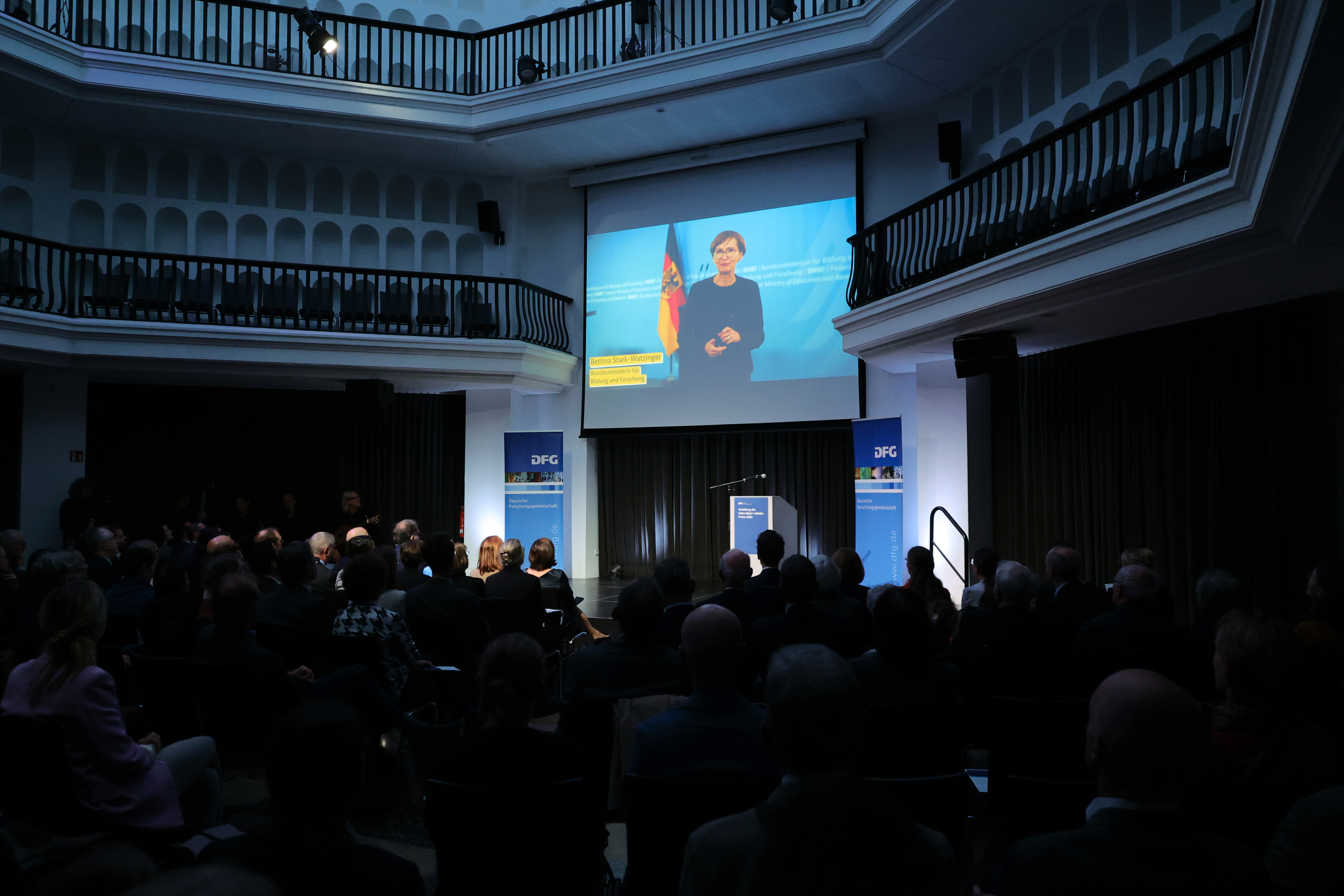 Videobotschaft der Bundesministerin Bettina Stark-Watzinger auf der Leinwand über dem Publikum