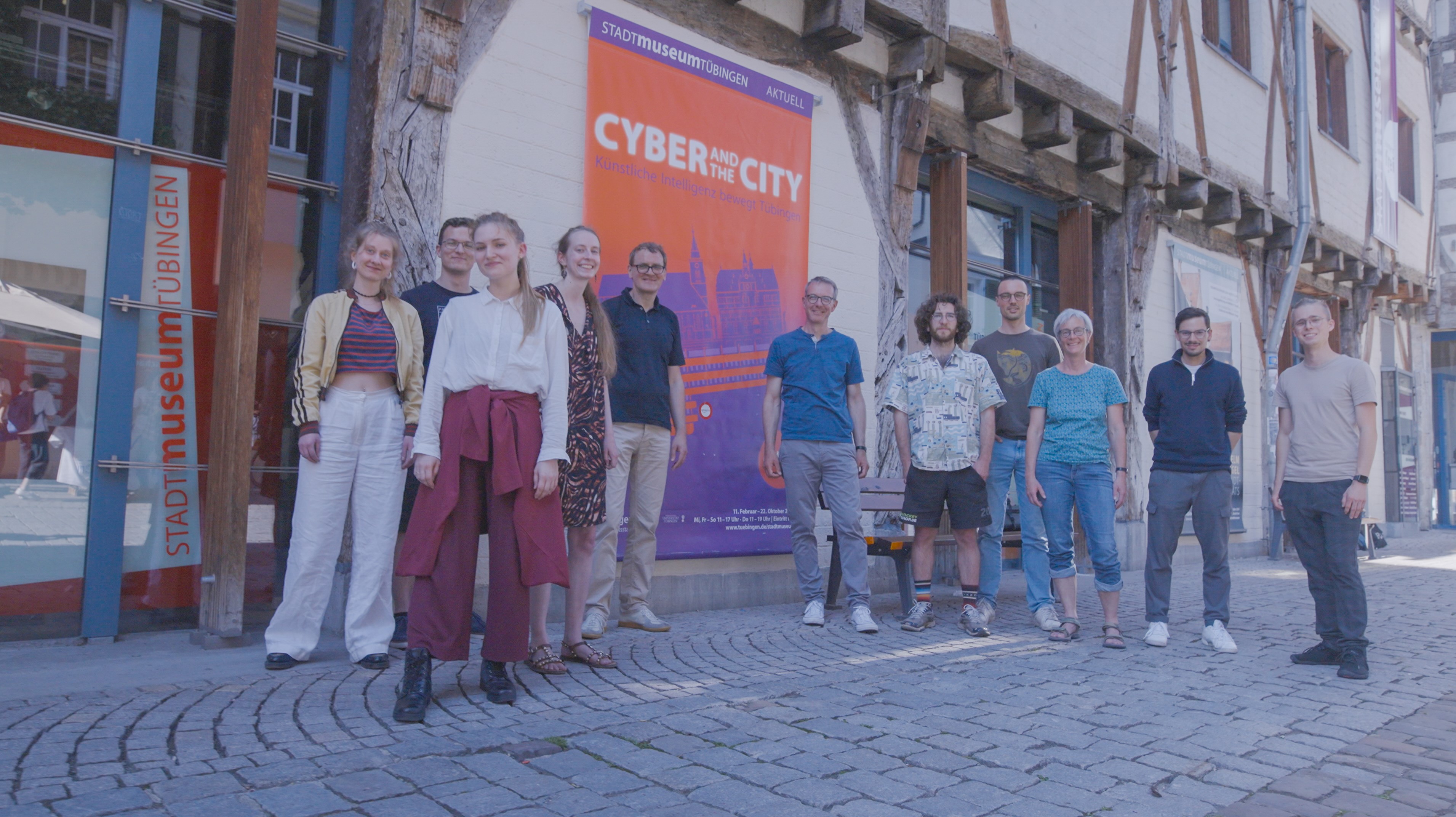 Gruppenbild des Teams "Cyber and the City" mit einem Plakat seiner Ausstellung im Stadtmuseum Tübingen