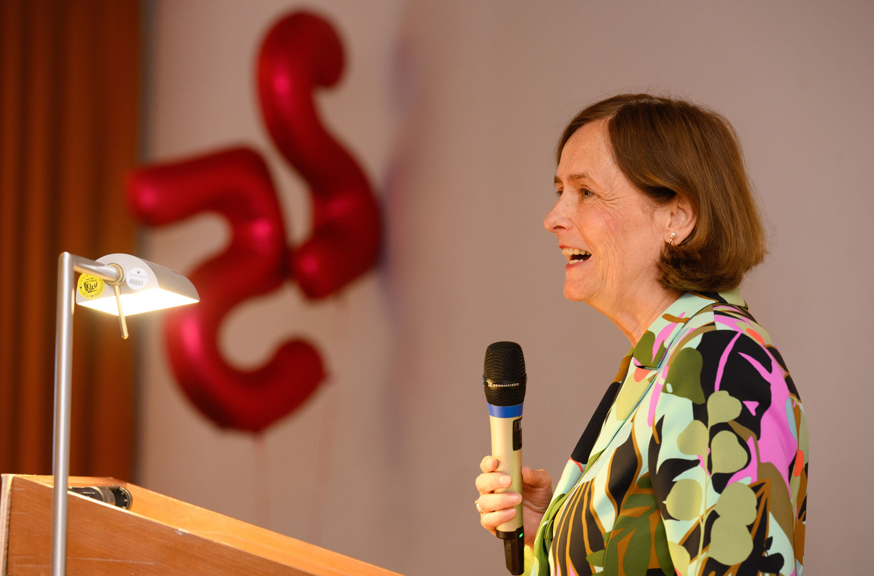DFG-Präsidentin Katja Becker am Rednerpult. Im Hintergrund zwei Luftballons mit den Zahlen des 25. Jubiläums "2" und "5"