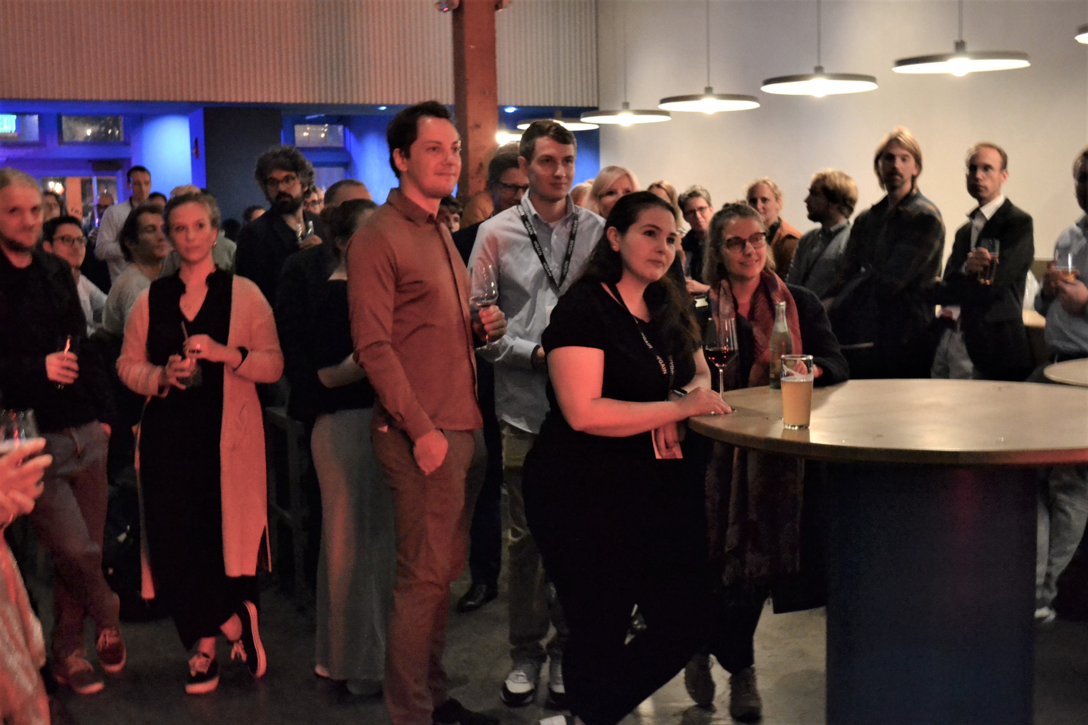 Several people stand around tables and listen to the program