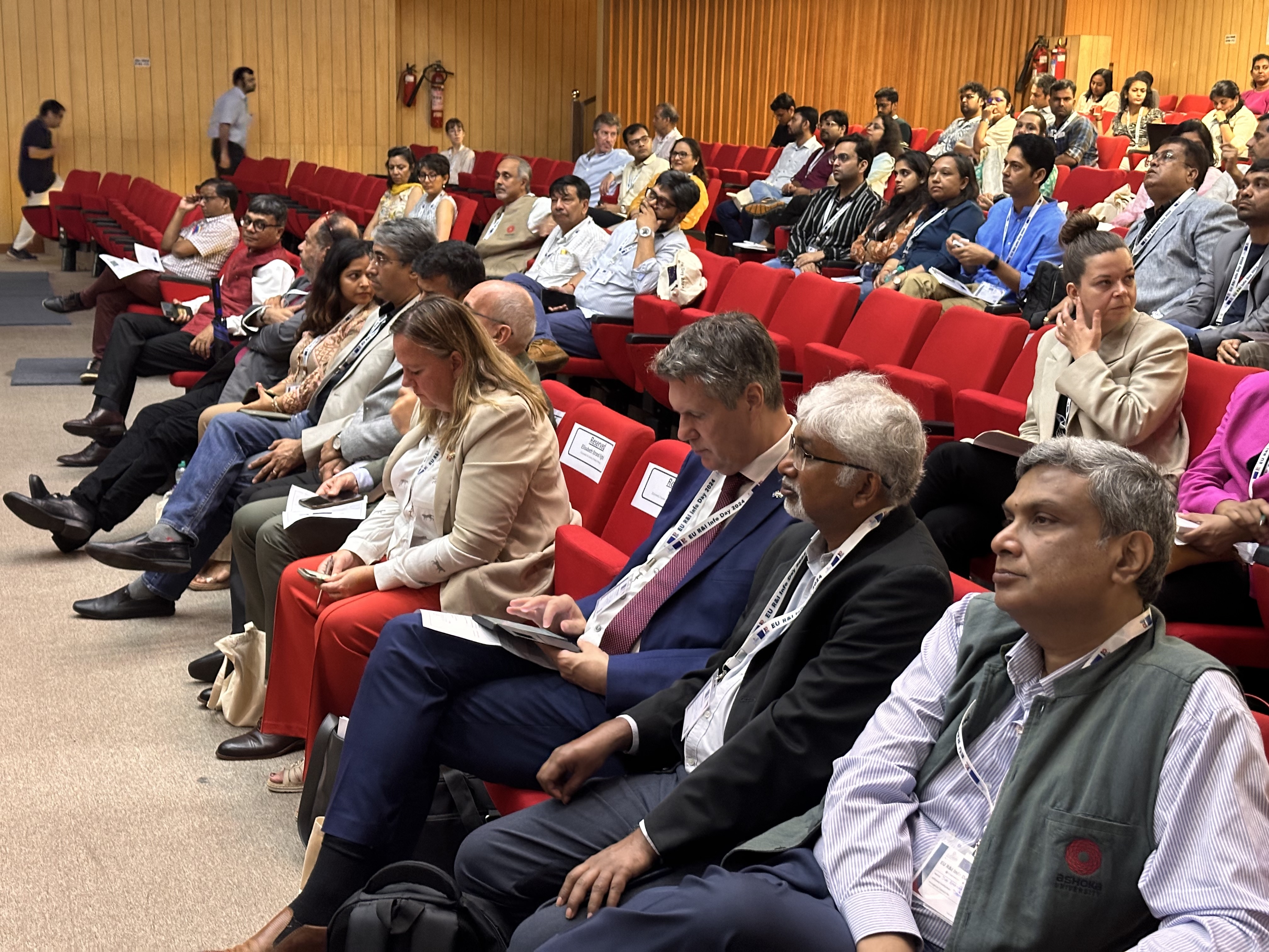 Participants are sitting in several rows of red chairs