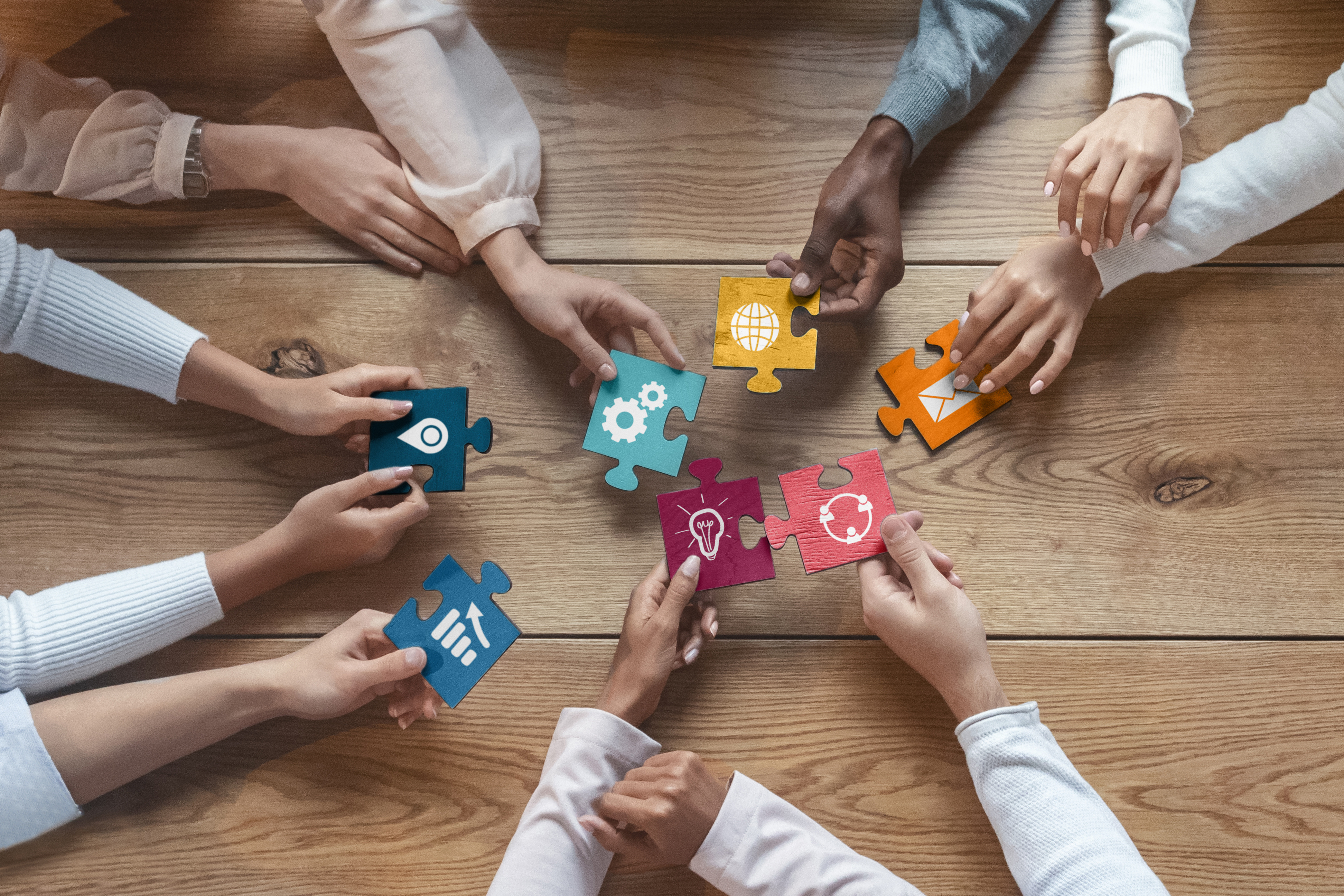 View from above on people holding puzzle pieces together on a table