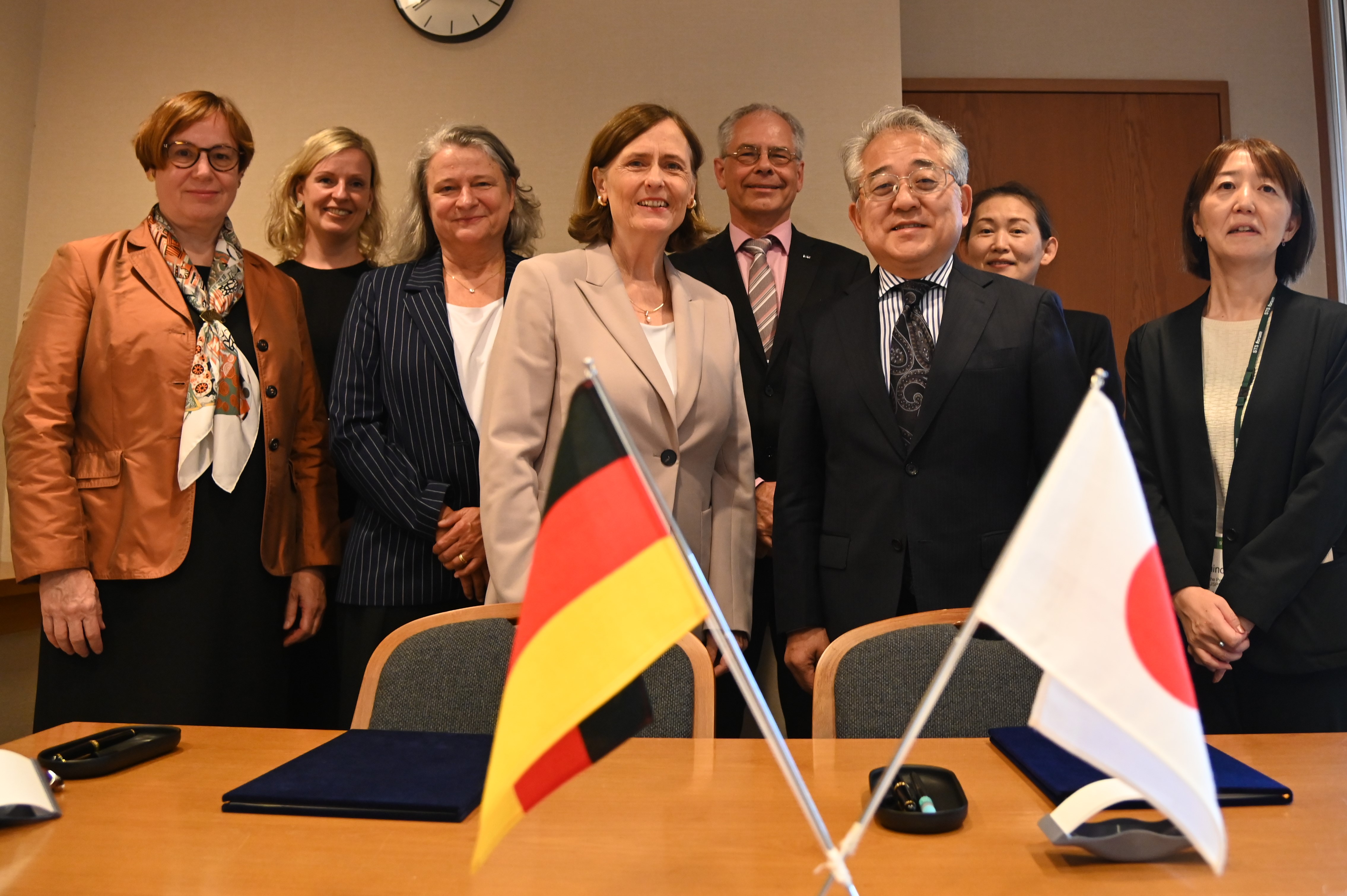 Die DFG-Delegation mit JSPS-Präsident stehen vor dem Tisch zur Unterzeichnung, davor sind Flaggen Deutschlands und Japans zu sehen.