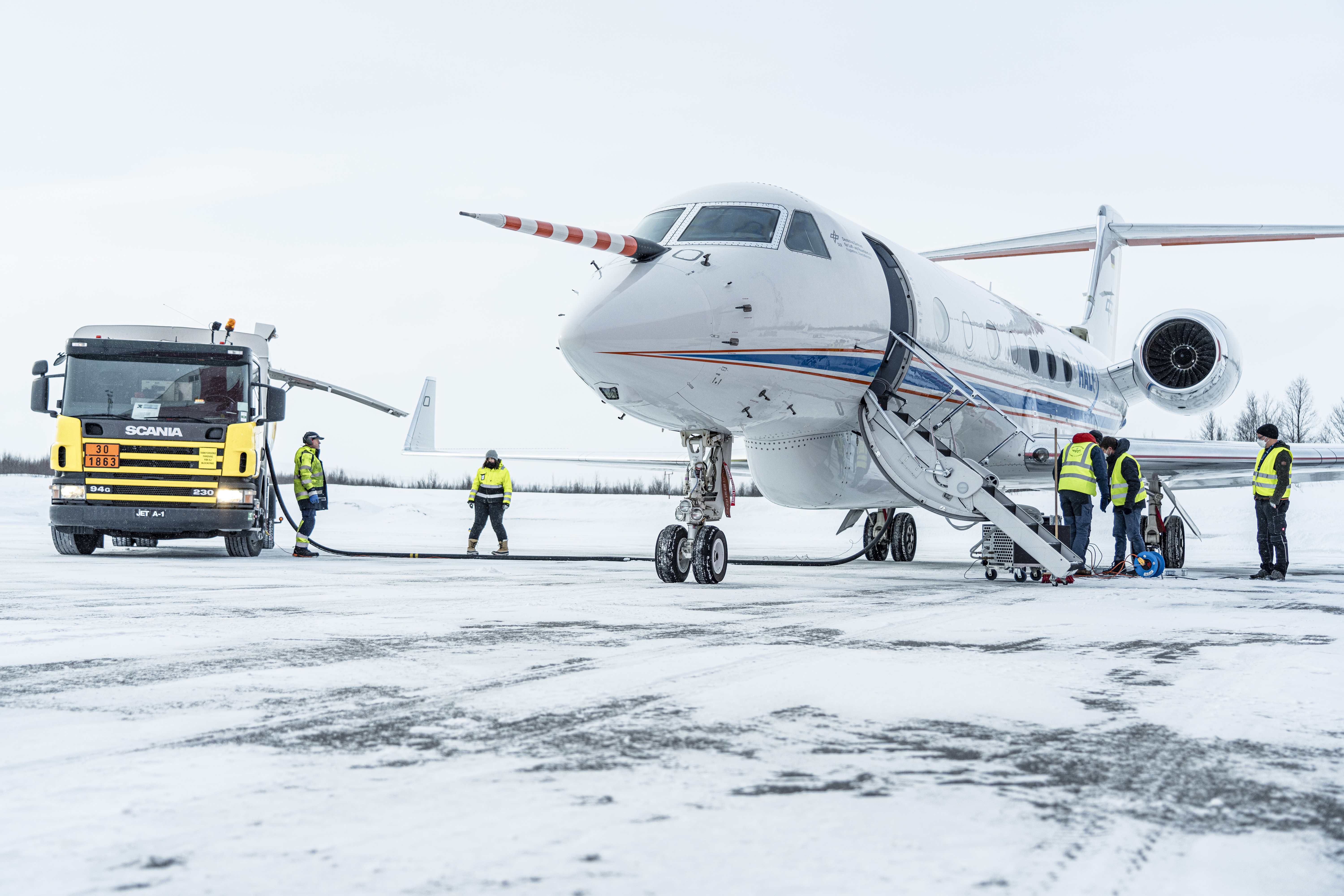 Das Forschungsflugzeug HALO und Mitarbeiter*innen stehen auf schneebedeckter Fläche.