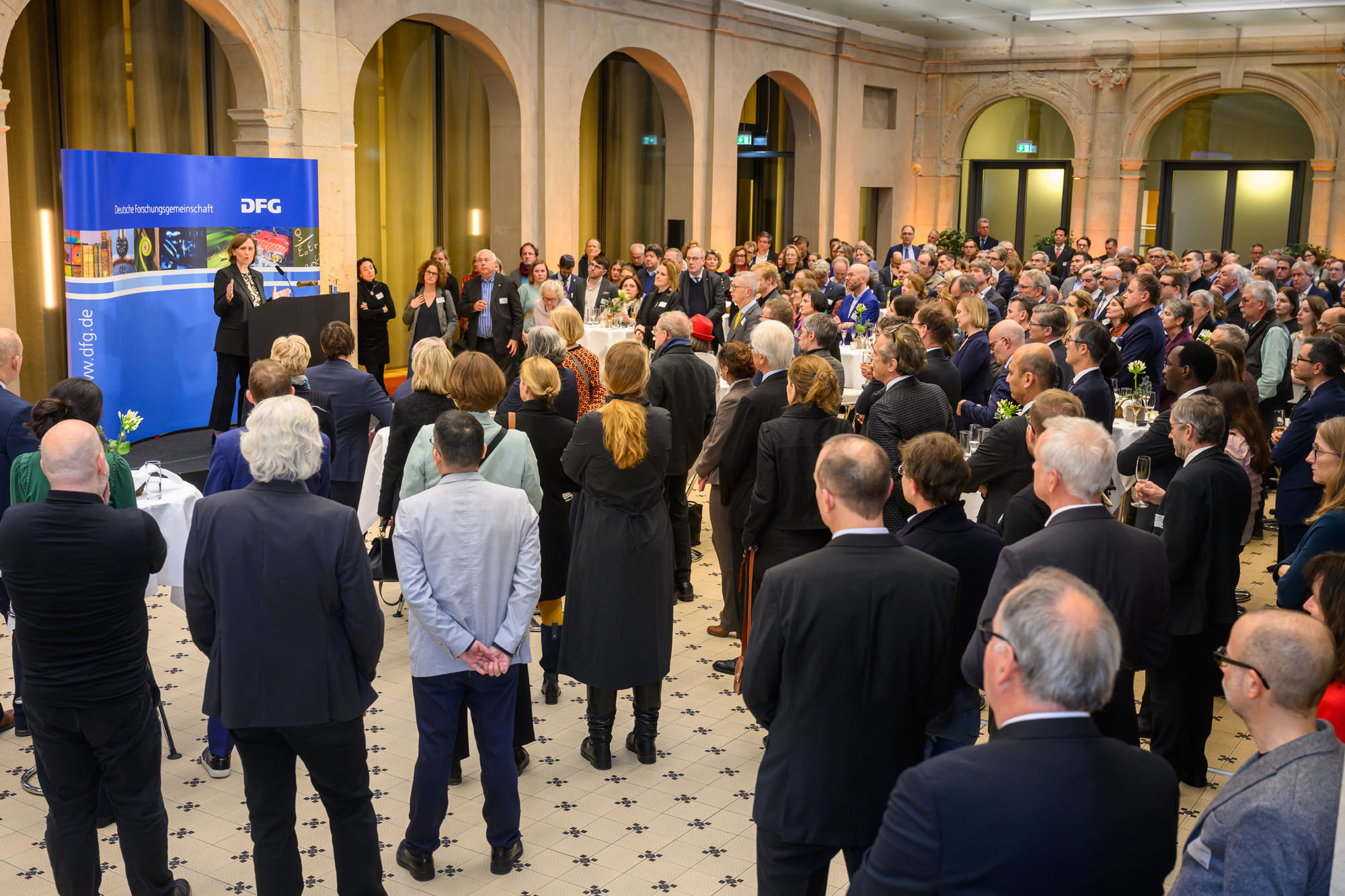 Die Gäste stehen im Leibnizsaal und sehen zum Rednerpult, vor dem Katja Becker spricht